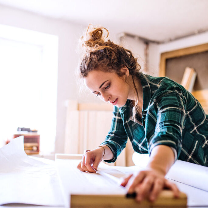 Small business of a young woman. Beautiful young woman worker in a workroom, measuring wood.